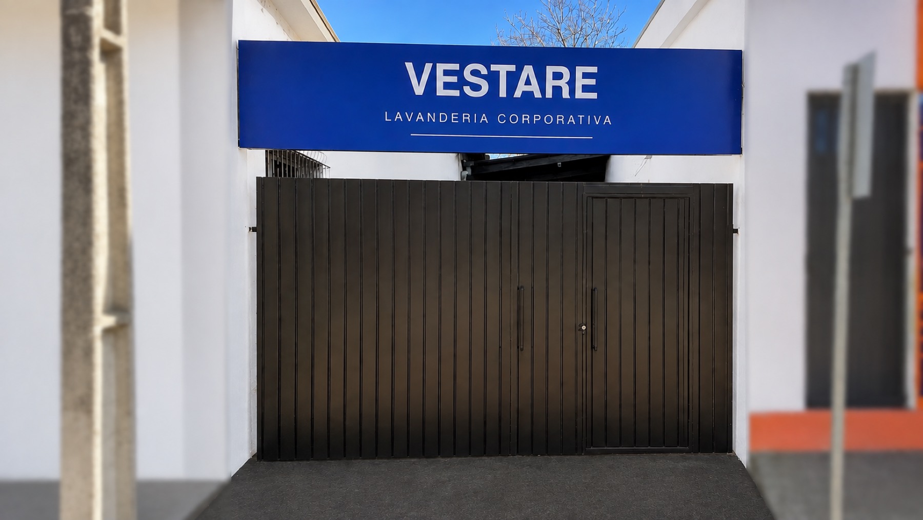 Entrada da Vestare: portão escuro sob uma placa azul com o nome Vestare Lavanderia Corporativa